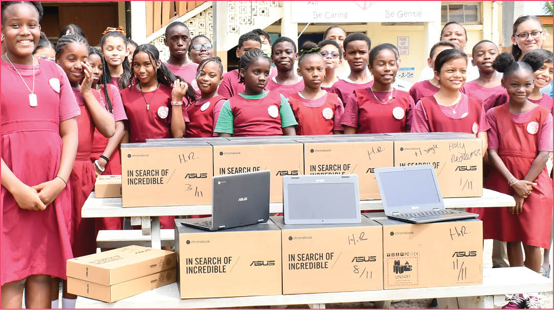 A group of children in red and white dresses are standing around a table with boxes on it. Description generated by AI